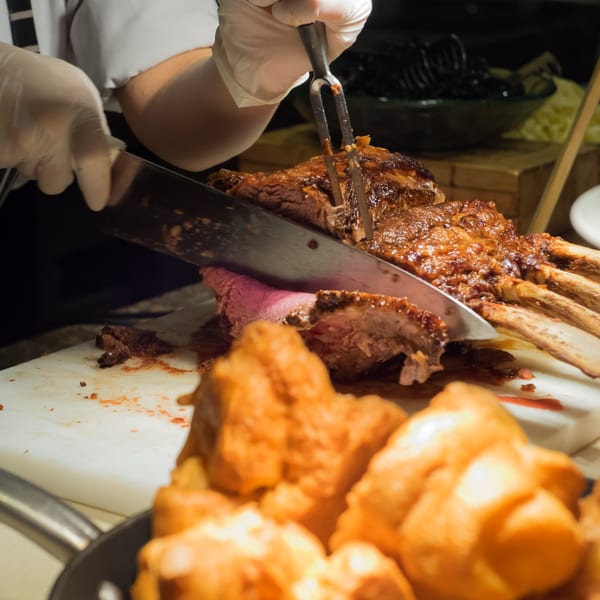 Gloved hands carving a large, juicy rack of BBQ ribs on a white cutting board.